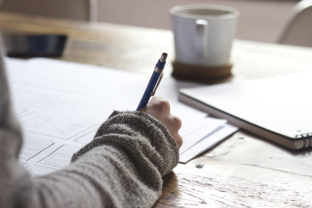 コーヒーを片手に手帳へ書き込む様子